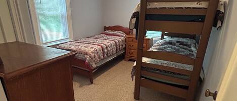 A bedroom with a bunk bed, a desk, and a dresser.