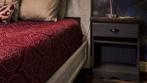 Une chambre à coucher avec une tête de lit en bois, une couvre-lit rouge à motifs et une table de chevet agrémentée d’une fresque murale sur le thème de l’espace.