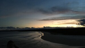 Een strand bij zonsondergang met een rustige zee en de silhouet van een persoon.