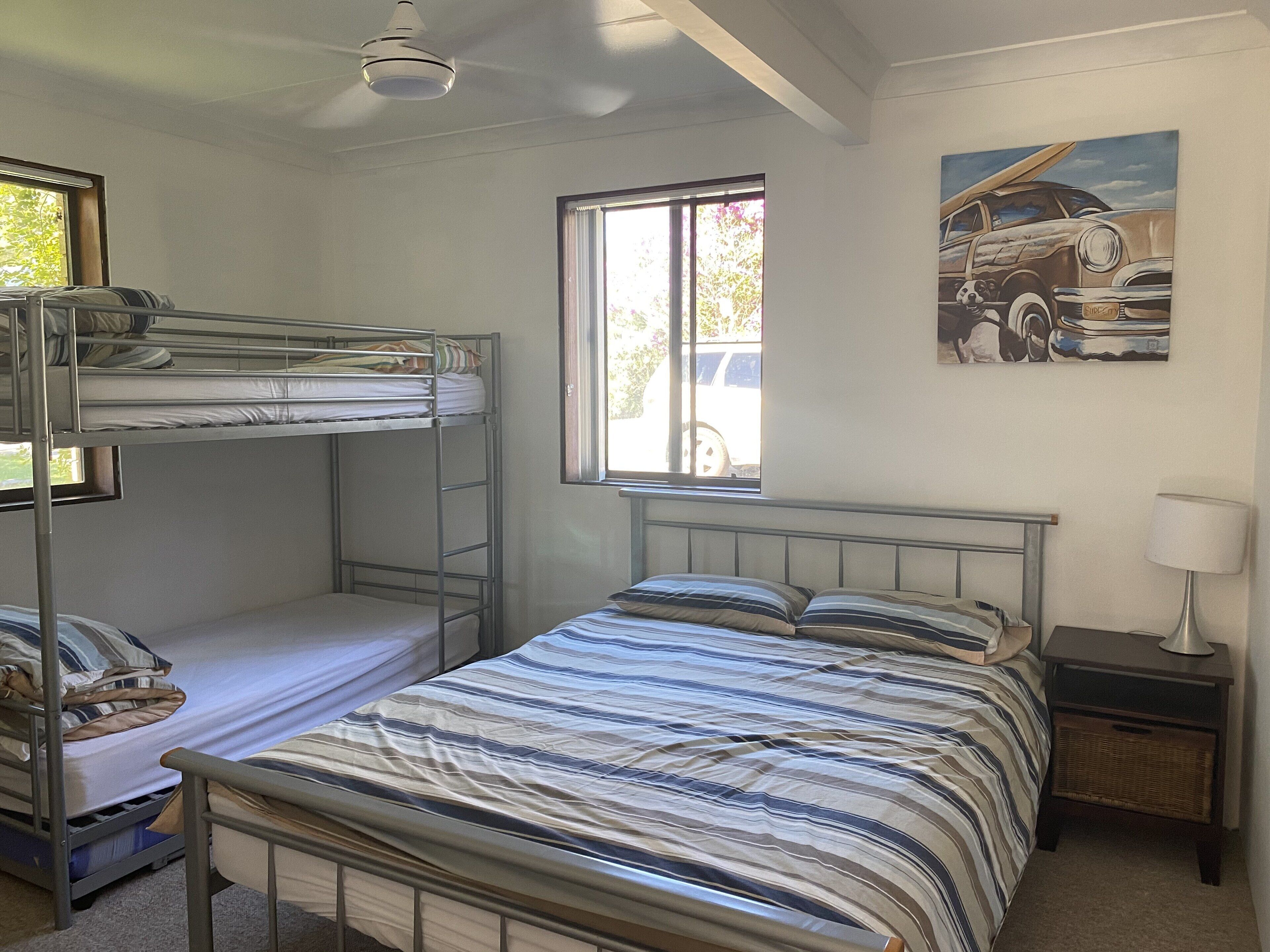 Habitación con literas, una ventana, un cuadro y una mesita de noche con lámpara.