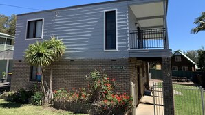 Een huis met twee verdiepingen, een balkon, een bakstenen fundering en een kleine tuin met rode bloemen.