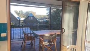 Een balkon met een houten tafel en twee stoelen, met uitzicht op een meer en huizen.