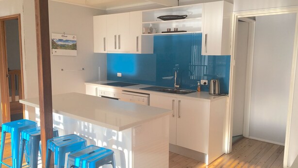 Een moderne keuken met witte kastjes, een blauwe spatwand en een klein eiland met krukken.