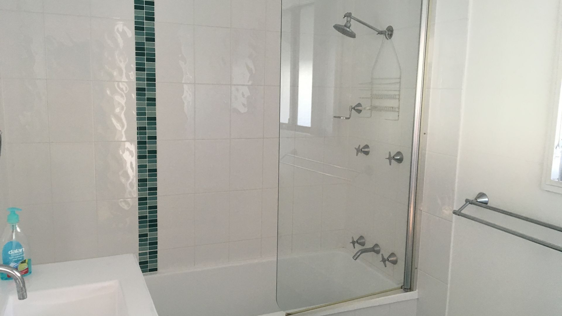 A modern bathroom with a glass shower enclosure, a white sink, and a green-tiled accent wall.