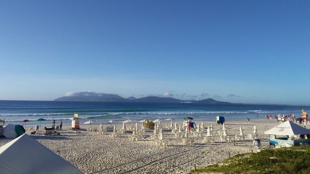 A beach with umbrellas and beach chairs, a clear sky, and mountains in the background. - Come and enjoy this paradise in a comfortable 3-bedroom apartment on Forte beach. (Centro)