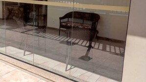 A glass-walled room with a bench and a chair, tiled floor, and a visible door. - Come and enjoy this paradise in a comfortable 3-bedroom apartment on Forte beach. (Centro)