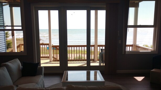A living room with a large glass door leading to a balcony overlooking the beach. - Loving Life at the Lake (Black River)