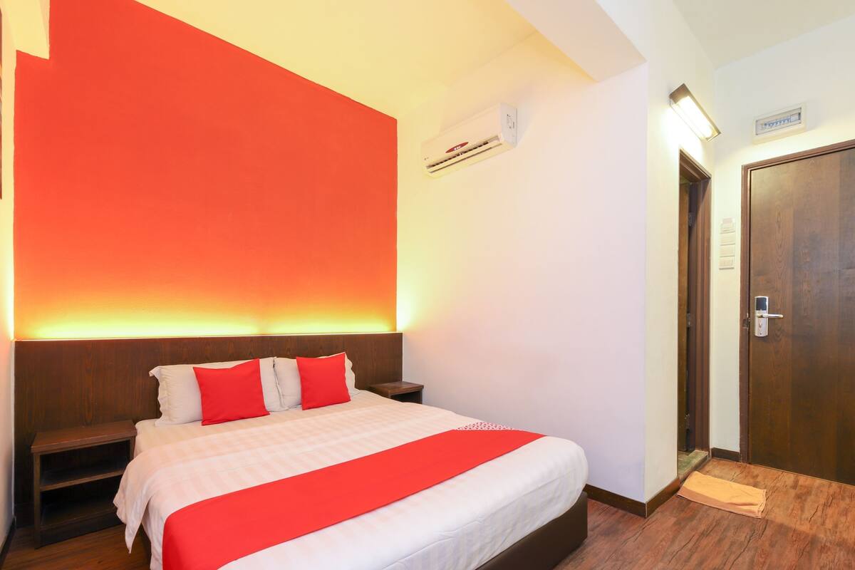 Een hotelkamer met een groot bed, een nachtkastje, een houten vloer en een deur met een handgreep.