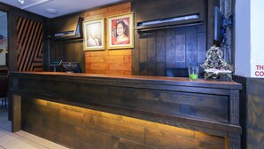 Una recepción con encimera de madera, dos retratos enmarcados encima, un adorno pequeño en el mostrador y una cámara de seguridad en el techo.