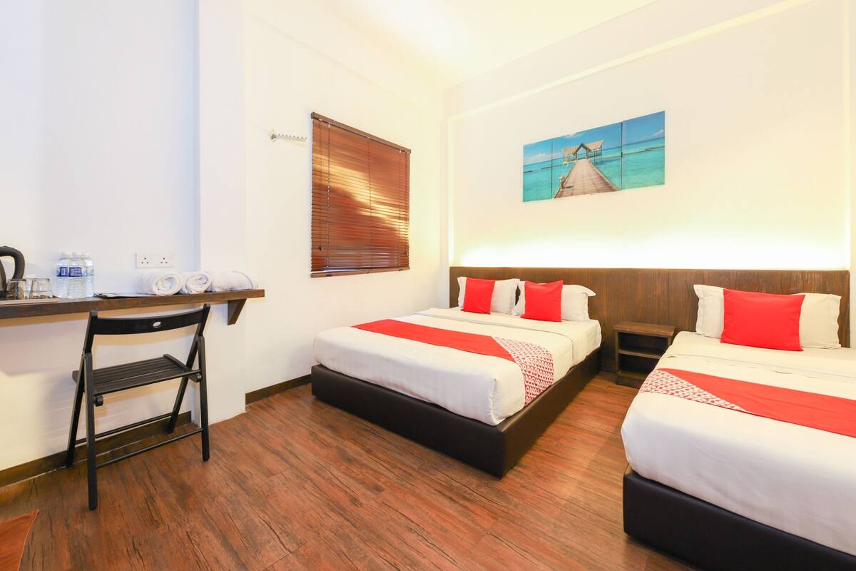 Een hotelkamer met twee bedden, een bureau, een stoel en een raam met jaloezieën.