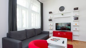 En moderne stue med en grå sofa, en rød lænestol, et hvidt sofabord, et rødt skab og et fladskærms-tv monteret på en hvid væg.