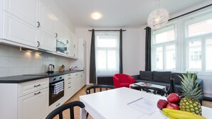 Et moderne køkken med hvide skabe, et spisebord med stole og en opholdsstue med sofa og sofabord.