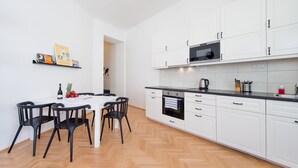 Et moderne køkken med hvide skabe, en sort bordplade og et spiseområde med et hvidt bord og sorte stole.