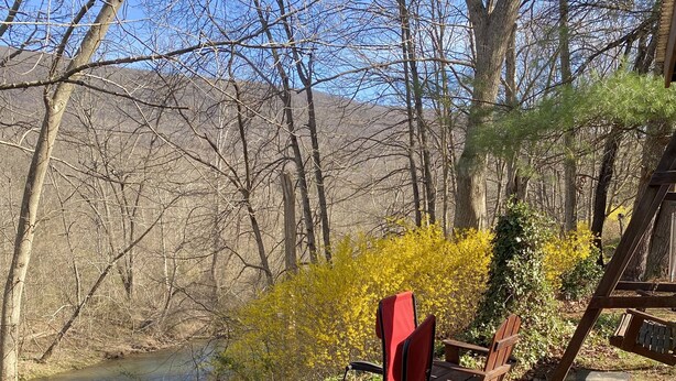 A campsite with a wooden deck, a red folding chair, and a view of a river and forest.