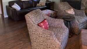 A living room with a brown leather sofa, patterned armchairs, a small round table, and a stone fireplace.