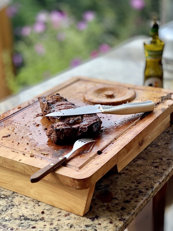 A steak on a wooden cutting board with a knife and fork beside it, placed on a granite countertop. - Beautiful house in Albuquerque, stunning views, 2 suites, swimming pool and sauna. (Teresópolis)