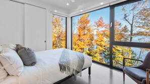 Une chambre moderne avec une grande fenêtre, un lit avec des oreillers et un fauteuil.