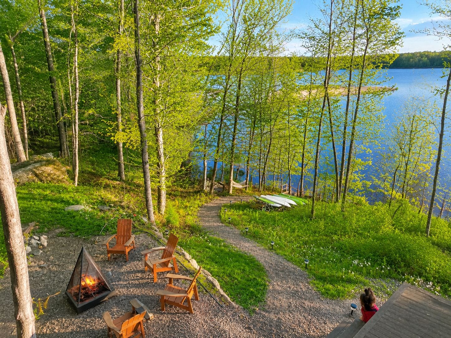 Un espace extérieur aménagé au bord du lac, avec un foyer, des chaises et une vue sur le lac.