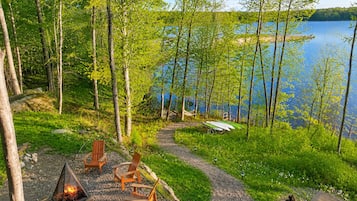 Un espace extérieur aménagé au bord du lac, avec un foyer, des chaises et une vue sur le lac.