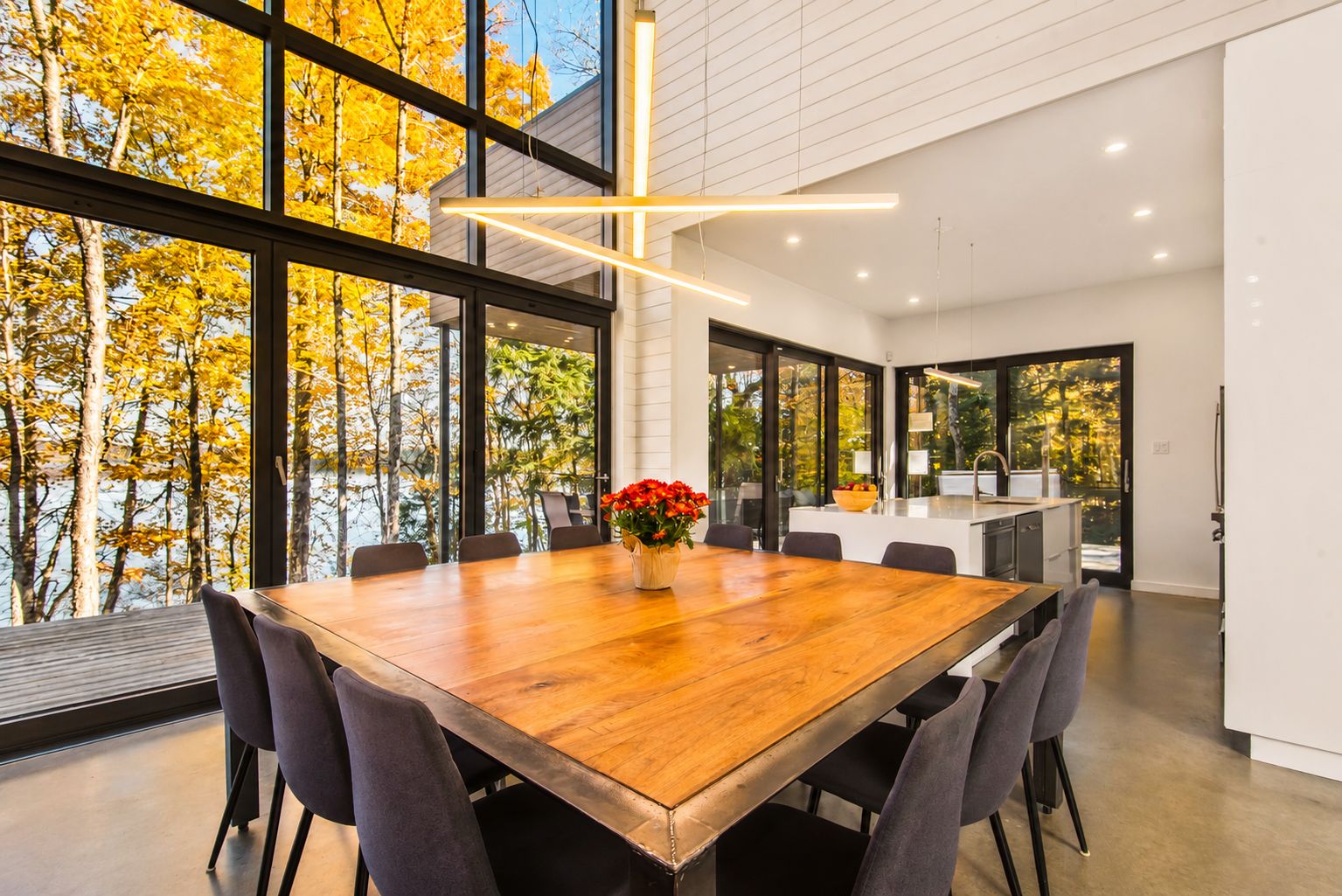 Un comedor moderno con una gran mesa de madera, sillas y un jarrón de flores rojas.