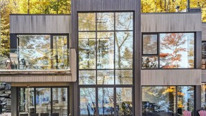 Un bâtiment moderne à deux étages, doté de grandes fenêtres qui reflètent les arbres et d’un patio aménagé avec des sièges extérieurs.