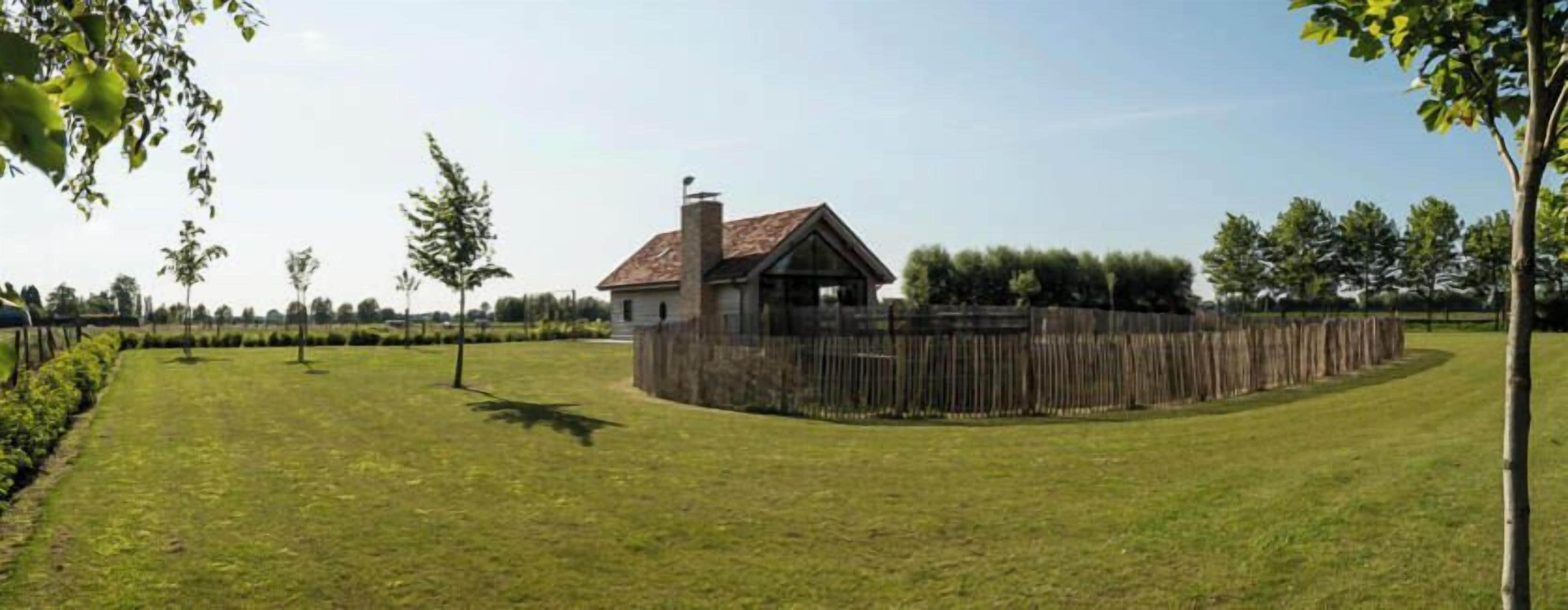 Une maison avec une cour clôturée, entourée d’arbres et sous un ciel dégagé.