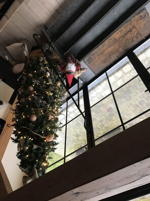 A Christmas tree with lights and ornaments, a window with a view of a stone building, and a wooden ceiling.