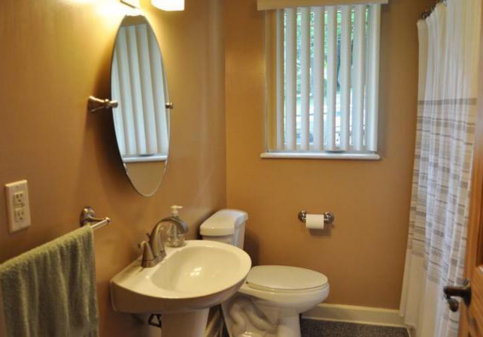 A bathroom with a sink, toilet, and a window with blinds.