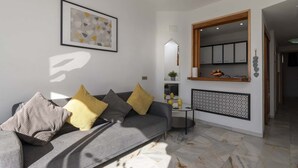 A modern living room with a grey sofa, yellow and grey cushions, a framed abstract artwork, a small side table with decorative items, and a large mirror. - Altamira 1 - One Bed with sea and pool view (Costa Adeje)
