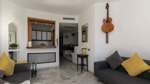 A modern living room with a grey sofa, yellow cushions, a black side table, and a guitar on the wall. - Altamira 1 - One Bed with sea and pool view (Costa Adeje)