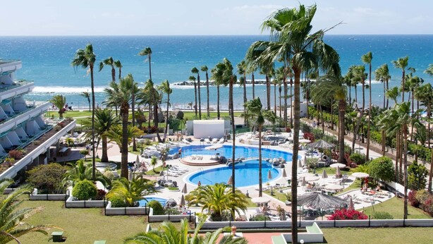 A resort with a central pool, palm trees, and a view of the ocean. - Altamira 1 - One Bed with sea and pool view (Costa Adeje)