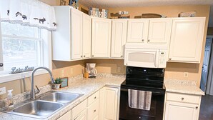 A kitchen with white cabinets, a stainless steel sink, a coffee maker, and a black oven. - Charming home with direct lake access, close to town (Greenville)