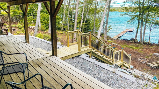 A wooden deck with a wooden staircase leading to a dock over water, surrounded by trees. - Charming home with direct lake access, close to town (Greenville)
