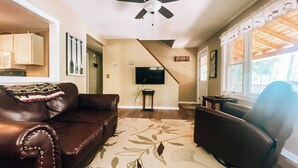 A living room with a brown leather couch, a black armchair, a ceiling fan, a flat-screen TV, and a staircase leading to another level. - Charming home with direct lake access, close to town (Greenville)