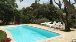 Ein rechteckiger Pool mit einer gefliesten Liegefläche und weißen Liegestühlen darum.