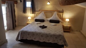 Ein ordentlich bezogenes Bett mit floralem Überwurf, zwei Nachttischlampen und einem Fenster mit Vorhängen.