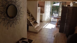 Ein geräumiges Wohnzimmer mit Treppe zu einem Balkon, einem Essbereich mit Tisch und Stühlen sowie Blick ins Freie.