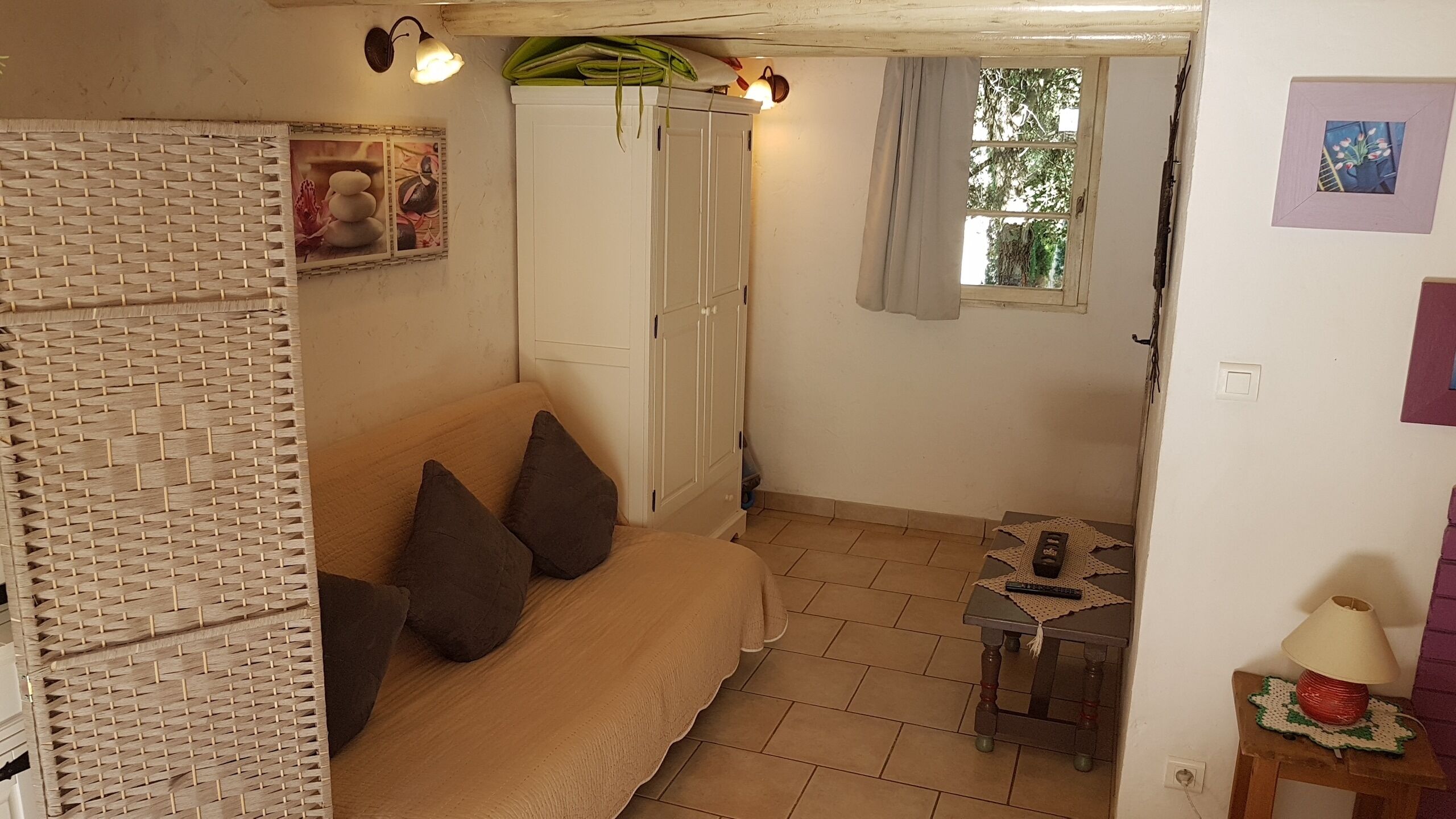 Une pièce confortable avec un canapé, une petite table sur laquelle se trouve une lampe, et une fenêtre avec des rideaux.