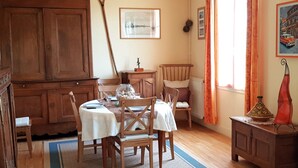 Un coin repas chaleureux, avec des meubles en bois, une table dressée pour deux personnes et une grande fenêtre agrémentée de rideaux.
