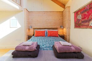 Une chambre confortable avec un plafond en bois, une couvre-lit à motifs et deux coussins rouges.