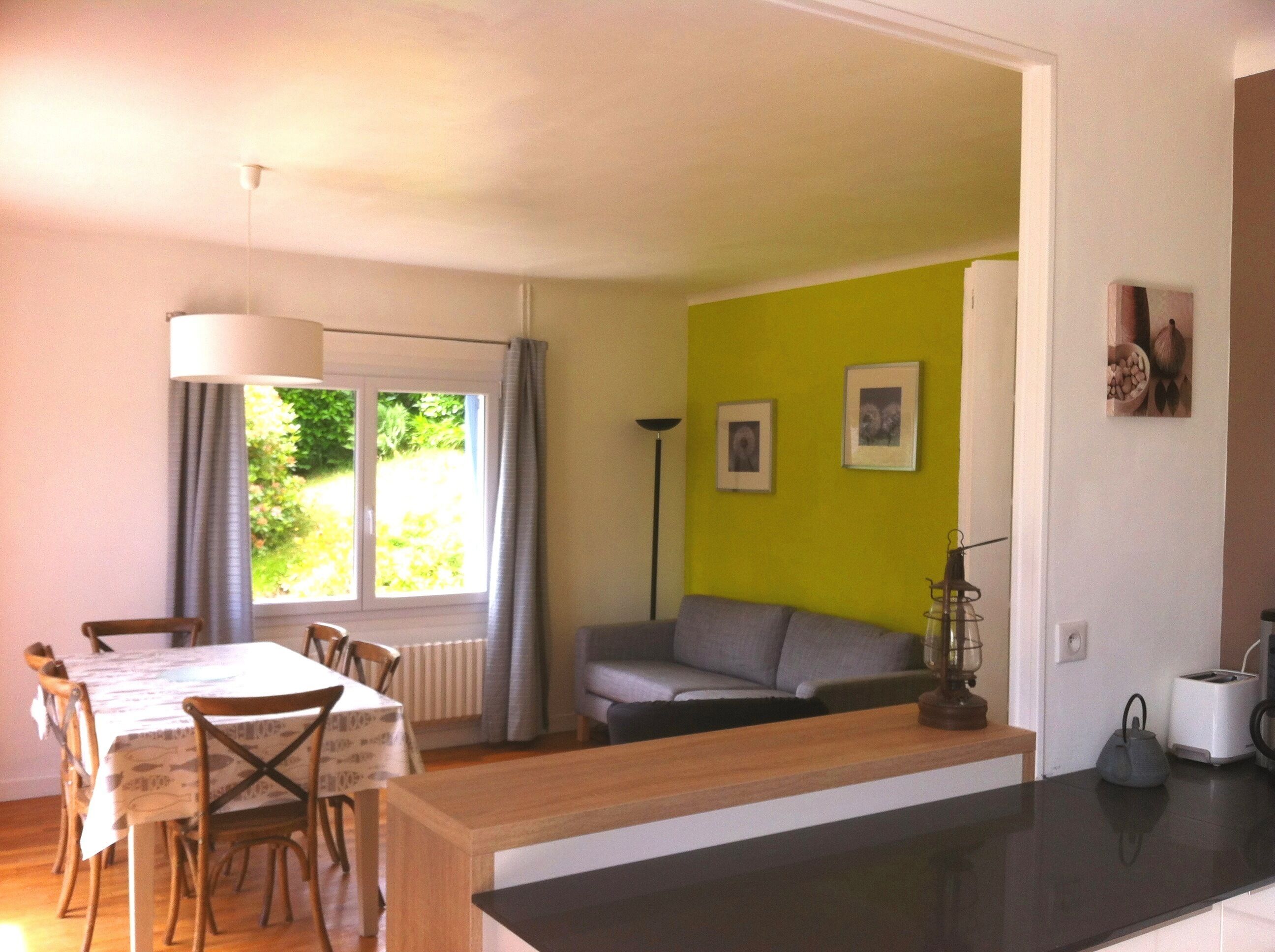 Un coin repas avec une table et des chaises, un canapé, une lampe sur pied, et un coin cuisine équipé d’un grille-pain et d’une bouilloire.