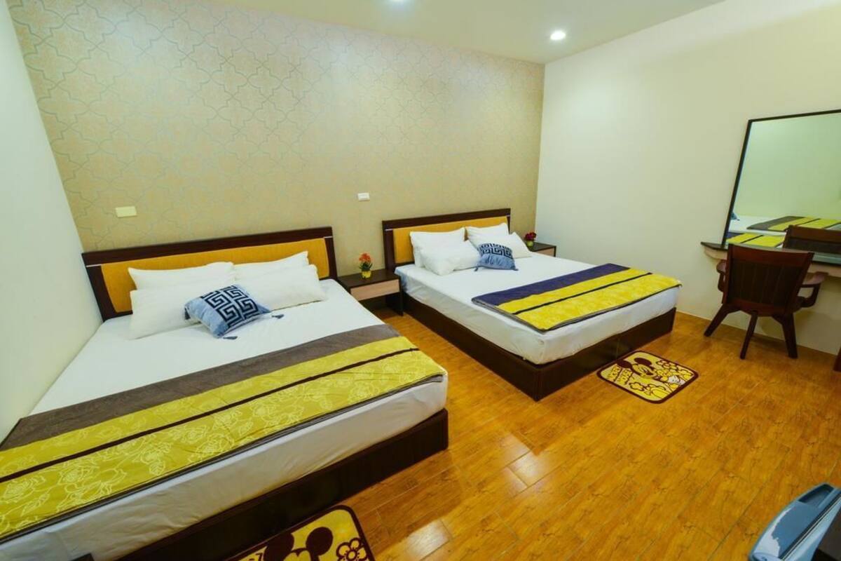 Habitación de hotel con dos camas, suelo de madera, un escritorio y un espejo.
