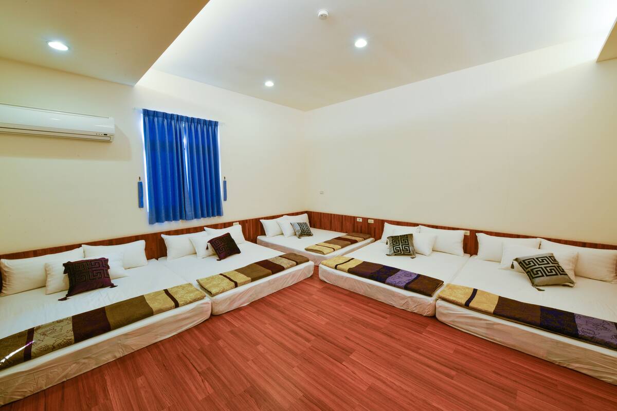 Habitación de hotel con dos camas individuales, suelo de madera, unidad de aire acondicionado y ventana con cortinas azules.