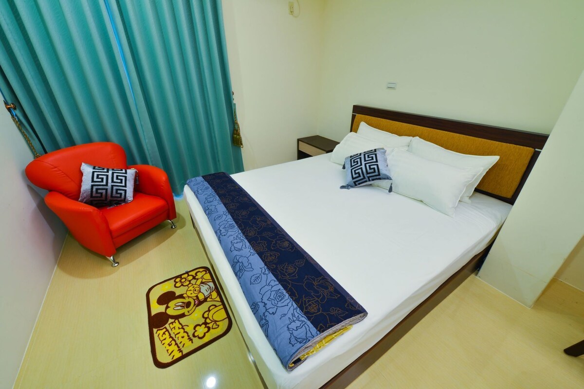 A hotel room with a bed, a red armchair, a nightstand, and a decorative rug.
