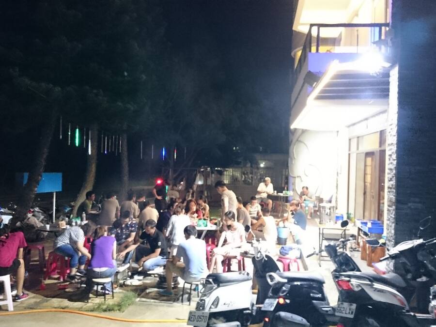 A crowded outdoor area with people sitting and standing, surrounded by parked motorcycles.