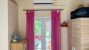 Ein Zimmer mit Holzboden, einer Schiebetür mit rosa Vorhängen, einem Kleiderschrank und einer Klimaanlage.