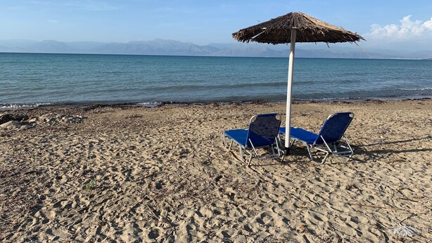 Ein Strand mit zwei blauen Liegestühlen und einem Strohdachschirm.
