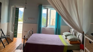 Ein Schlafzimmer mit einem Bett, einem fensterbeprägten Fenster, Blick ins Freie und einer Holzbalkendecke.