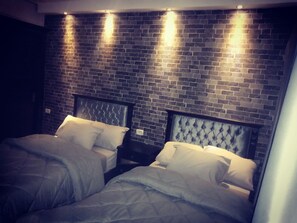 A room with two beds, each with a headboard and white bedding. The walls are made of dark brick, and there are three wall-mounted lights. - Cairo Castle Hostel (Cairo)