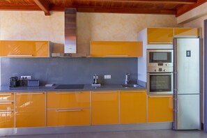 A kitchen with orange cabinets, a stainless steel refrigerator, a microwave, and an oven.
